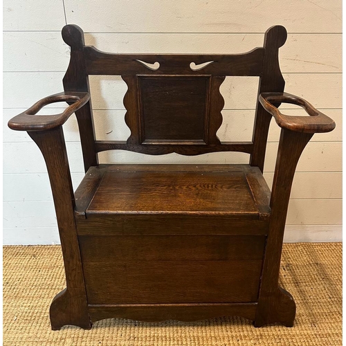 135 - An oak Arts and Crafts hall stand bench with hinged lid to reveal storage and a carved back