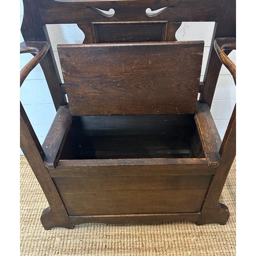 135 - An oak Arts and Crafts hall stand bench with hinged lid to reveal storage and a carved back