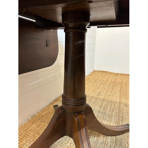 145 - A mahogany drop leaf dining table on turned central support on four reeded splayed legs and brass ca... 