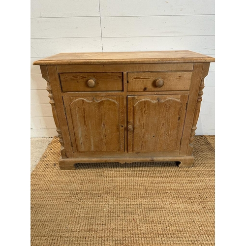 198 - A pine two drawer and two door cupboard with carved doors and supports AF (H76cm W100cm D43cm)