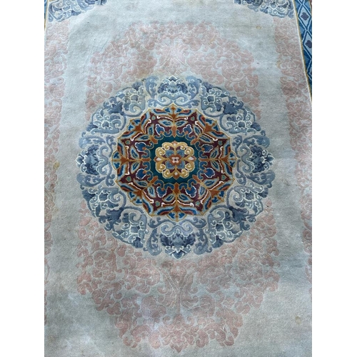 227 - A beige ground wool rug with geometric border and blue and red central medallion 280cm x 180cm