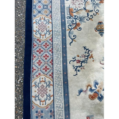 228 - A large beige ground rug with a blue boarder and central medallion 276cm x 386cm