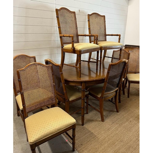 64 - An oval two leaf bamboo effect dining table and eight wicker back chairs, two of them being carvers ... 