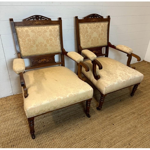 156 - A pair of inlaid and carved open arm chairs on turned legs and castors, upholstered in a beige flora... 