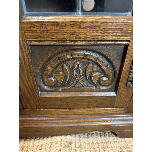 188 - An oak glazed media cabinet with leaded glass and carved detail to doors (H94cm W62cm D49cm)