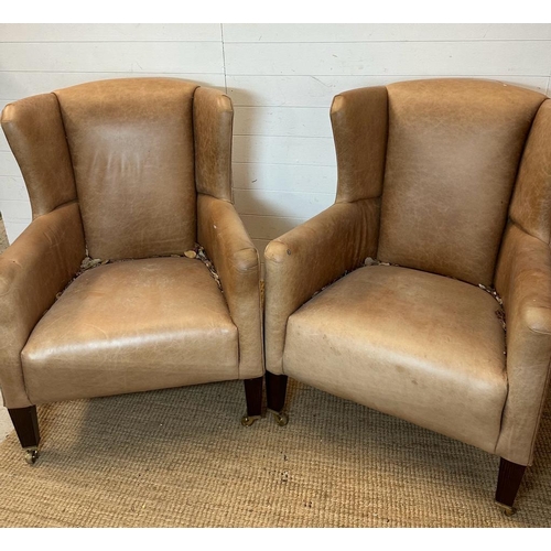 26 - A pair of wing back tan leather arm chairs with brass castors