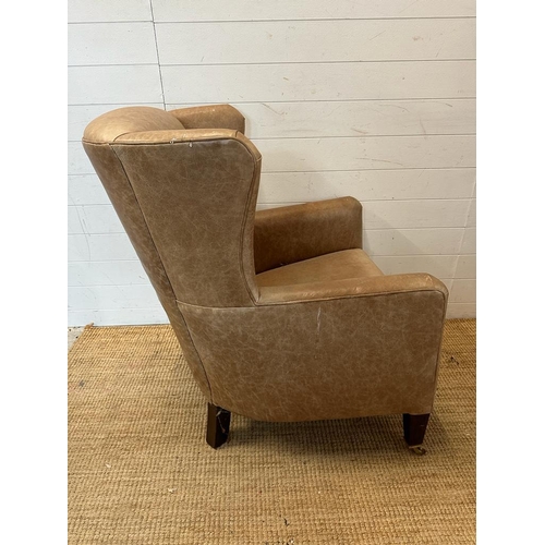 26 - A pair of wing back tan leather arm chairs with brass castors