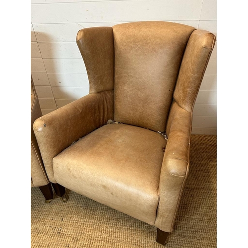 26 - A pair of wing back tan leather arm chairs with brass castors