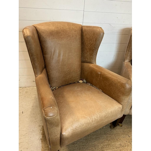 26 - A pair of wing back tan leather arm chairs with brass castors