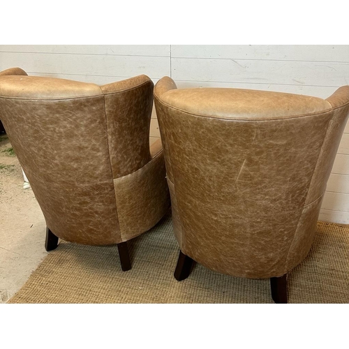 26 - A pair of wing back tan leather arm chairs with brass castors