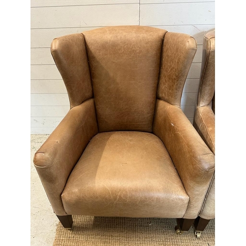 26 - A pair of wing back tan leather arm chairs with brass castors