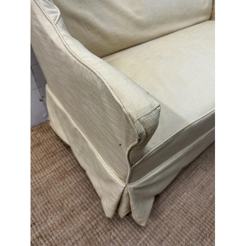 6 - A two seater cream upholstered skirted sofa