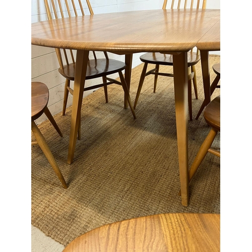 100 - A blondie Ercol circular drop leaf table with six stick back chairs (H72cm W124cm)