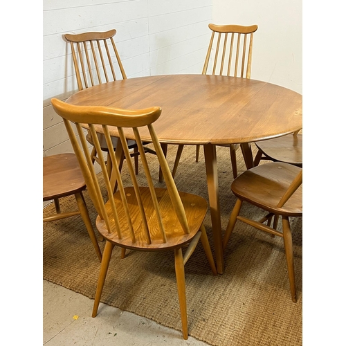 100 - A blondie Ercol circular drop leaf table with six stick back chairs (H72cm W124cm)