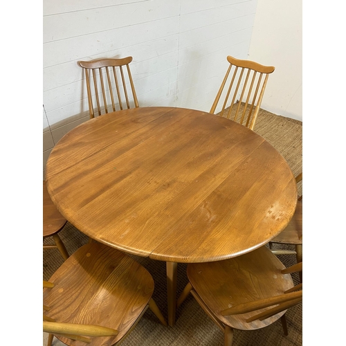 100 - A blondie Ercol circular drop leaf table with six stick back chairs (H72cm W124cm)