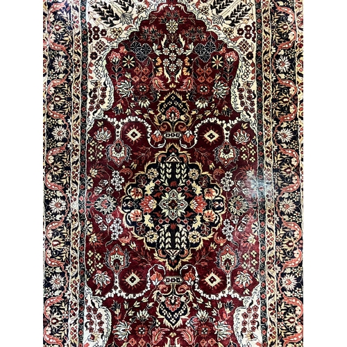 214 - A silk runner rug with red grounds and a scrolling and floral design to centre