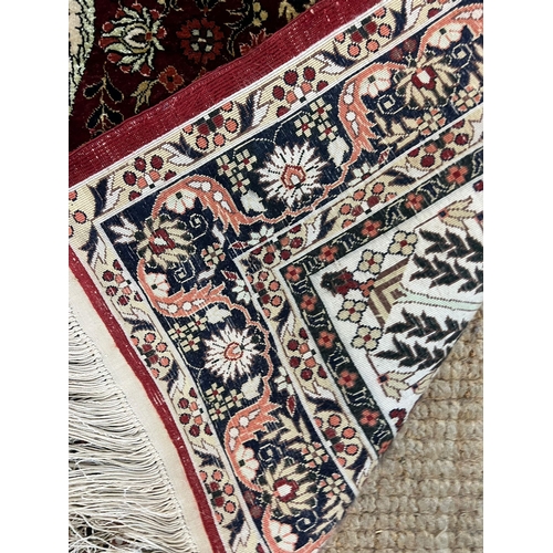 214 - A silk runner rug with red grounds and a scrolling and floral design to centre