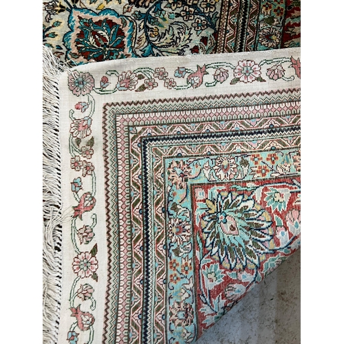 217 - A silk and wool carpet/rug with floral border of reds and greens and rectangular centre panel of sim... 