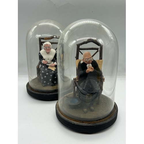 309 - A pair of papier mache lady and gentleman seated figures under glass domes and linths (H23cm)