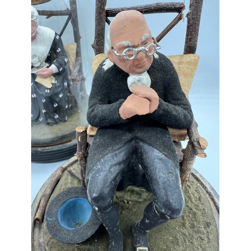 309 - A pair of papier mache lady and gentleman seated figures under glass domes and linths (H23cm)