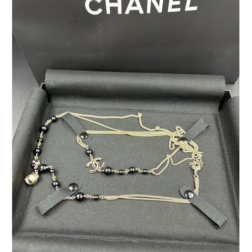 532 - A Chanel long fashion necklace, black and gold themed, boxed with bag.