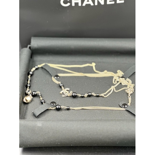 532 - A Chanel long fashion necklace, black and gold themed, boxed with bag.