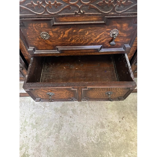 58 - An oak dresser base with two central drawers flanked by two cupboards with carved fronts and relief ... 