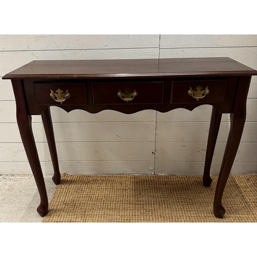 115 - A three drawer magnolia console table with brass drop down handles (H69cm W92cm D31cm)