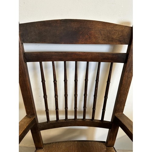 125 - An oak rush seated spindle back open arm chair in the Arts and Crafts style