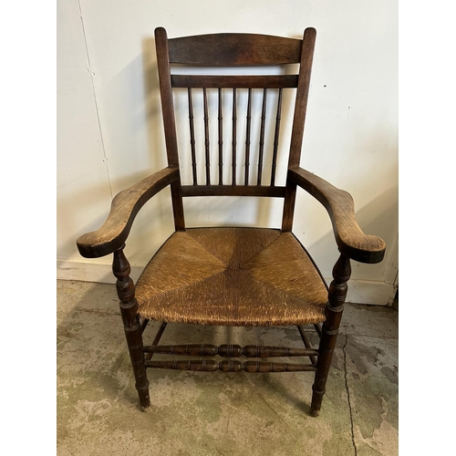 125 - An oak rush seated spindle back open arm chair in the Arts and Crafts style