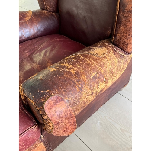 50 - An antique leather club chair in a distressed manner (H84cm W97cm SH37cm)