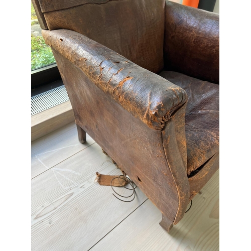 54 - An antique leather club chair in distressed manner with scrolling arms (H95cm W71cm D31cm SH43cm)Cro... 