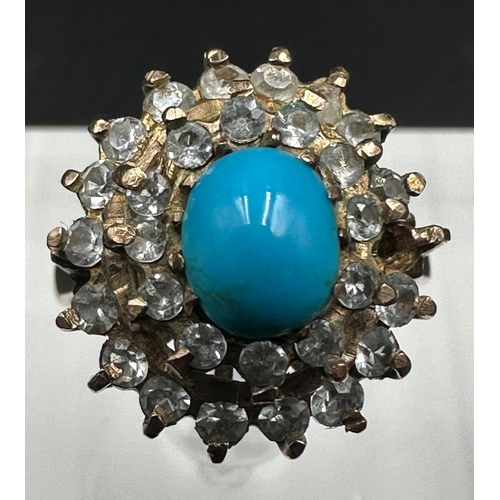 560 - A turquoise central stone ring surrounded by clear stones on gold metal setting. AF