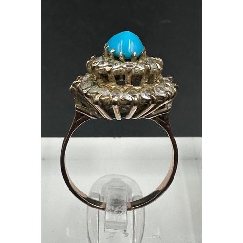 560 - A turquoise central stone ring surrounded by clear stones on gold metal setting. AF