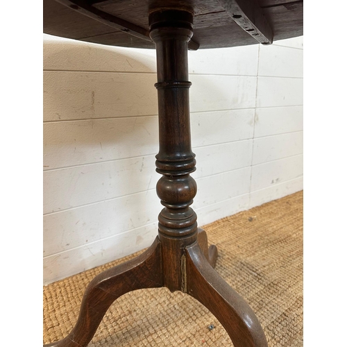 47 - A circular oak tilt top table on turned central support and splayed tripod legs (H66cm Dia71cm