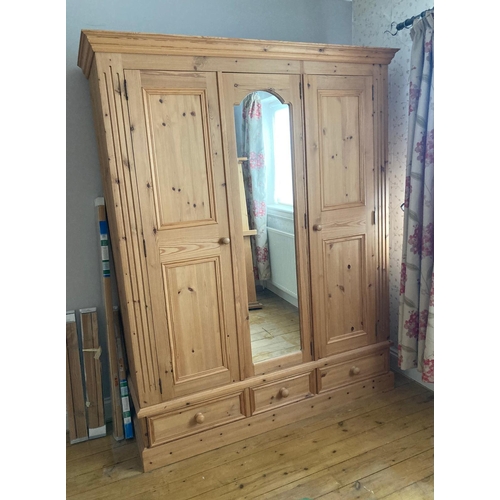 19 - A pine wardrobe comprising of central mirrored door flanked by two panel doors with three drawers un... 