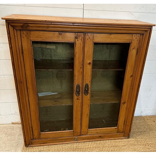 31 - A distress pine two door glazed cabinet opening to two shelves (H92cm D32cm W90cm)