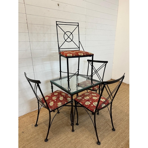 83 - A black wrought iron glass topped breakfast table and four accompanying chairs with red ground flora... 