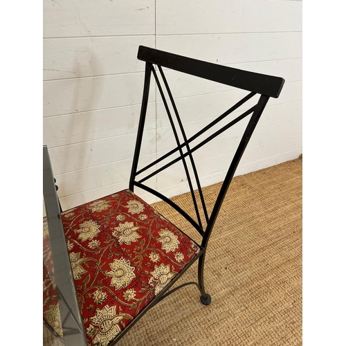 83 - A black wrought iron glass topped breakfast table and four accompanying chairs with red ground flora... 
