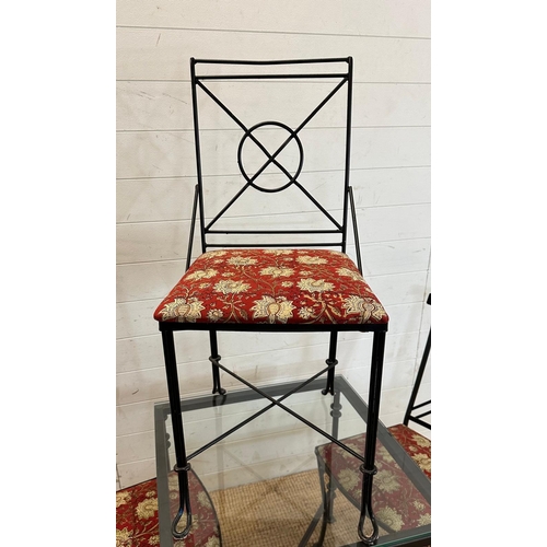 83 - A black wrought iron glass topped breakfast table and four accompanying chairs with red ground flora... 