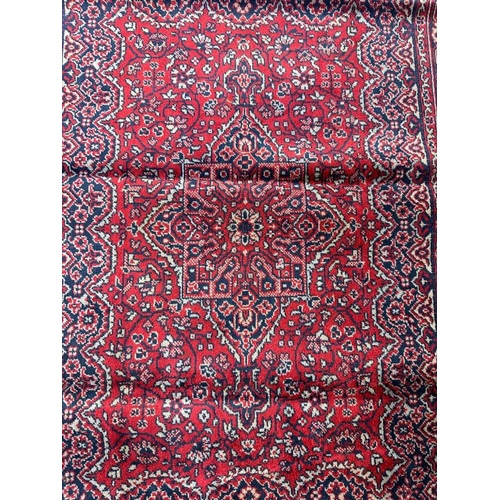 176 - A small red ground rug with geometric boarder and central shield 106cm x 67cm