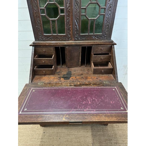 87 - A dark oak ornately carved book case bureau, the green glazed cupboard opening to central cupboard f... 