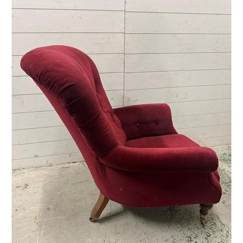 82 - A burgundy upholstered button back arm chair on castors