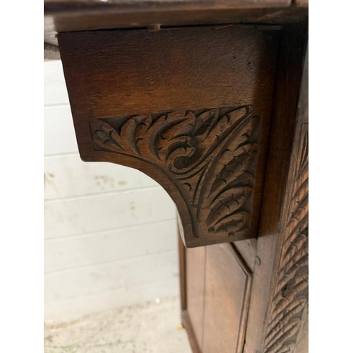 127 - An oak butlers companion or sideboard with heavily carved panels to front, comprising of single draw... 