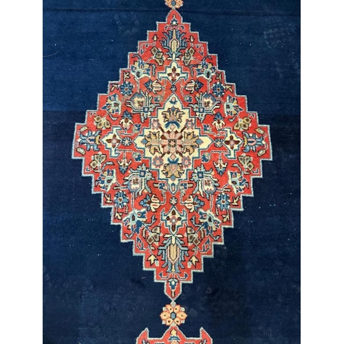 194 - A wool rug blue grounds with scrolling border and red central shield 340cm x 210cm