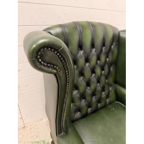 29 - A green faux leather wingback chair with a button-tufted back, cabriole legs and brass stud detailin... 