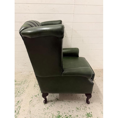 29 - A green faux leather wingback chair with a button-tufted back, cabriole legs and brass stud detailin... 