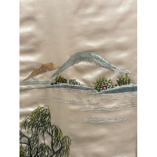 344 - A Japanese framed embroidered silk of a lakeside scene with mountains and a village to foreground, s... 