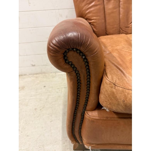 58 - A tan leather upholstered armchair with brass stud detail