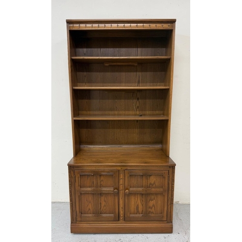 136 - An ercol mural wall unit in a golden dawn finish featuring an open bookcase over a two door cabinet ... 
